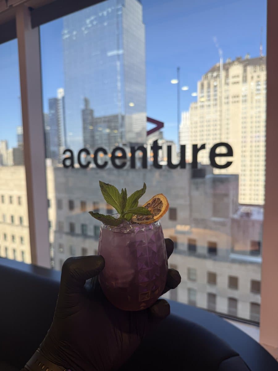 A garnished Abu Sauce mocktail held against the Accenture sign at a corporate rooftop event