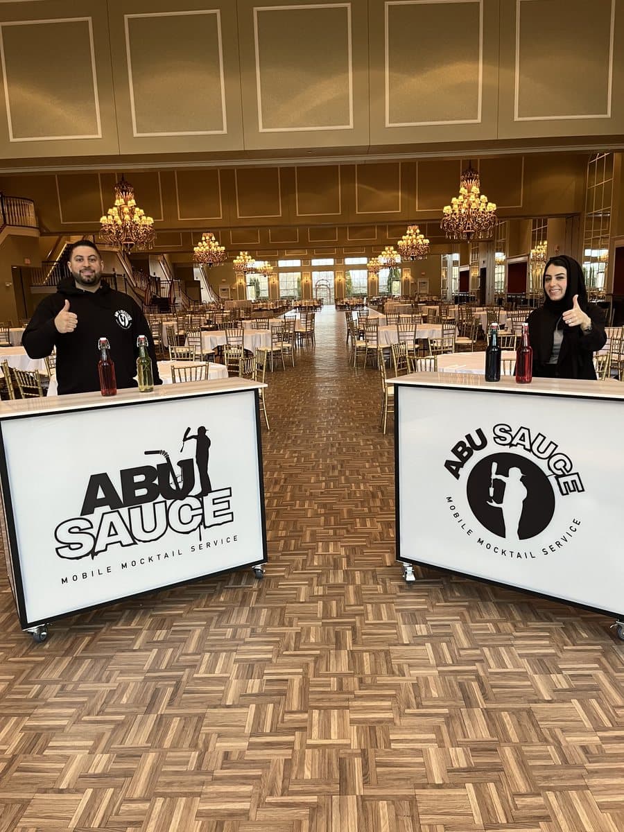 Two Abu Sauce mocktail bars set up in a chandelier-lit ballroom