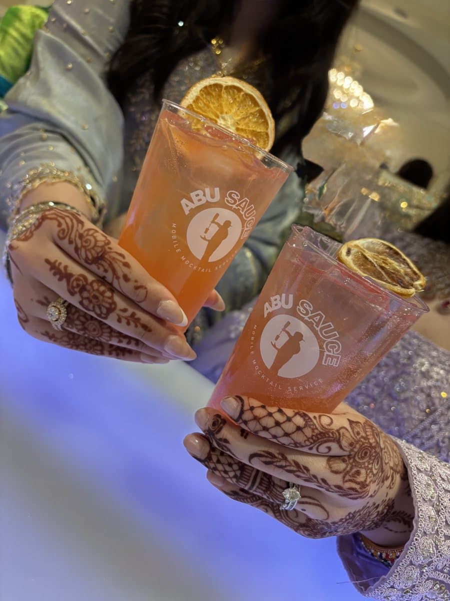 Two henna-decorated hands toasting with garnished Abu Sauce mocktails