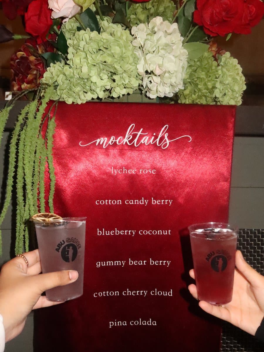 Two Abu Sauce mocktails in front of a mocktail menu framed by flowers