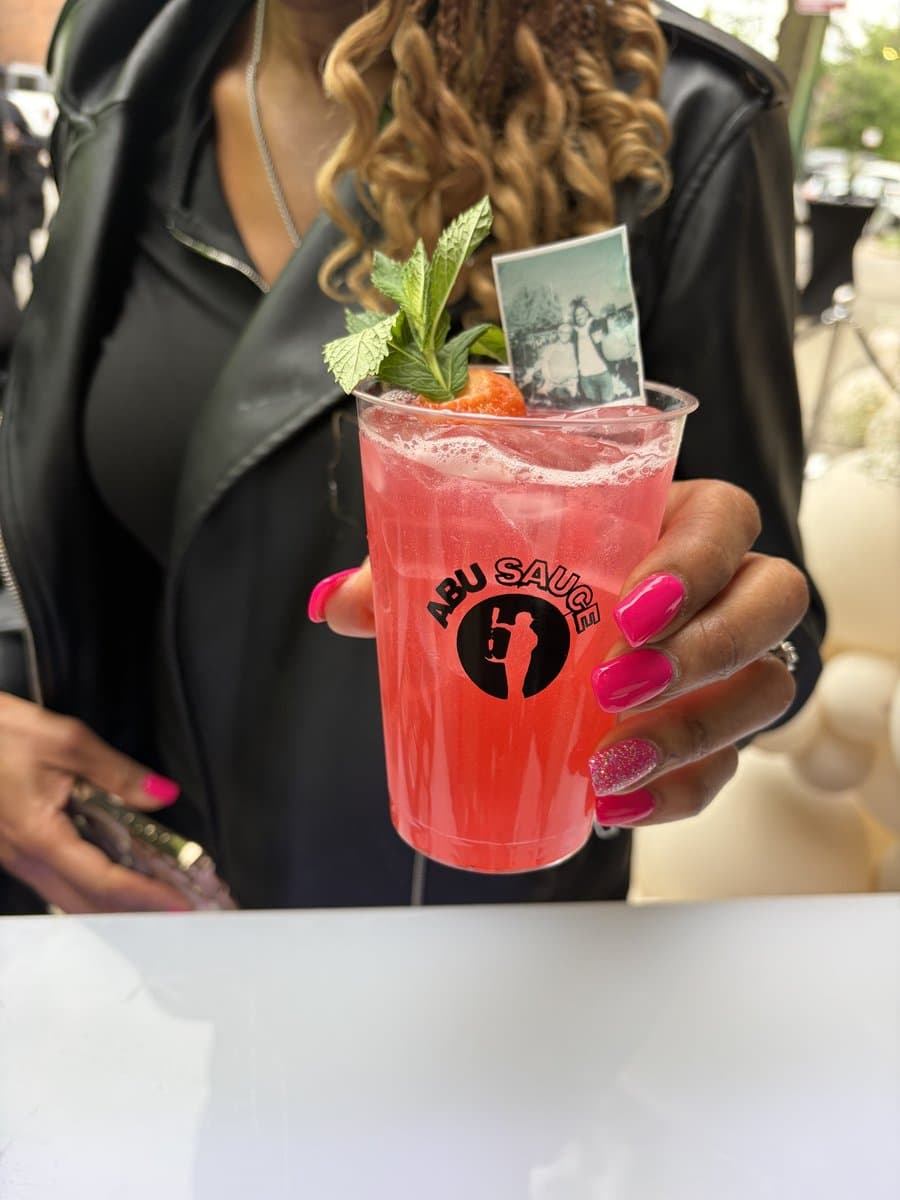 A guest holding a garnished Abu Sauce mocktail with a custom photo drink topper