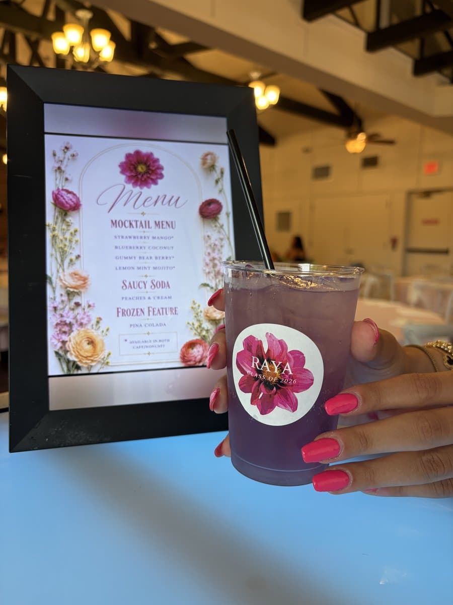 A purple Abu Sauce mocktail with a custom floral topper beside a framed event mocktail menu