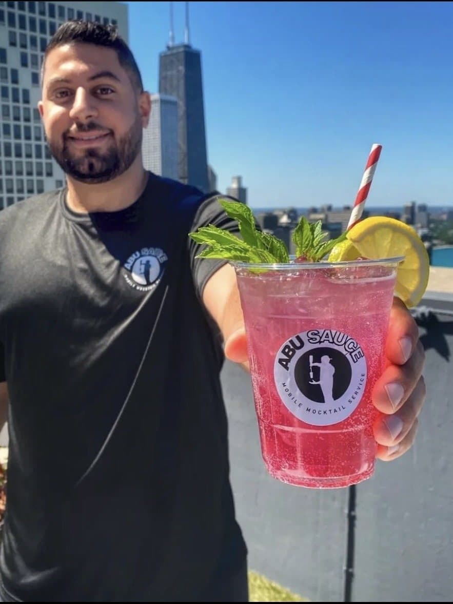 An Abu Sauce team member holding a garnished mocktail on a rooftop above the Chicago skyline