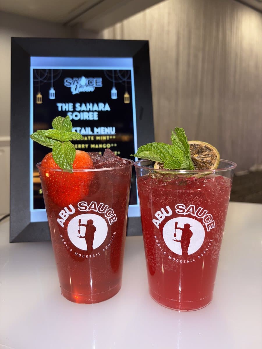 Two red Abu Sauce mocktails garnished with mint in front of a printed event mocktail menu