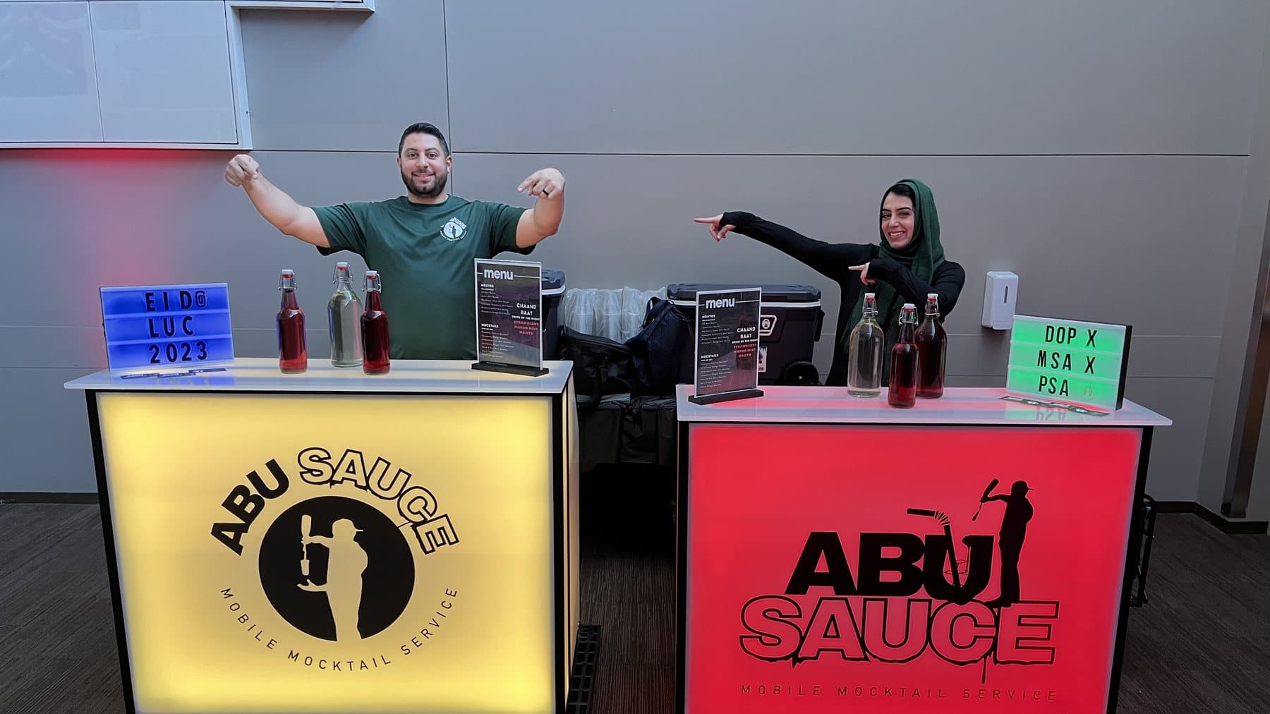 Nour and Fedaa behind the two lit Abu Sauce bars at an event