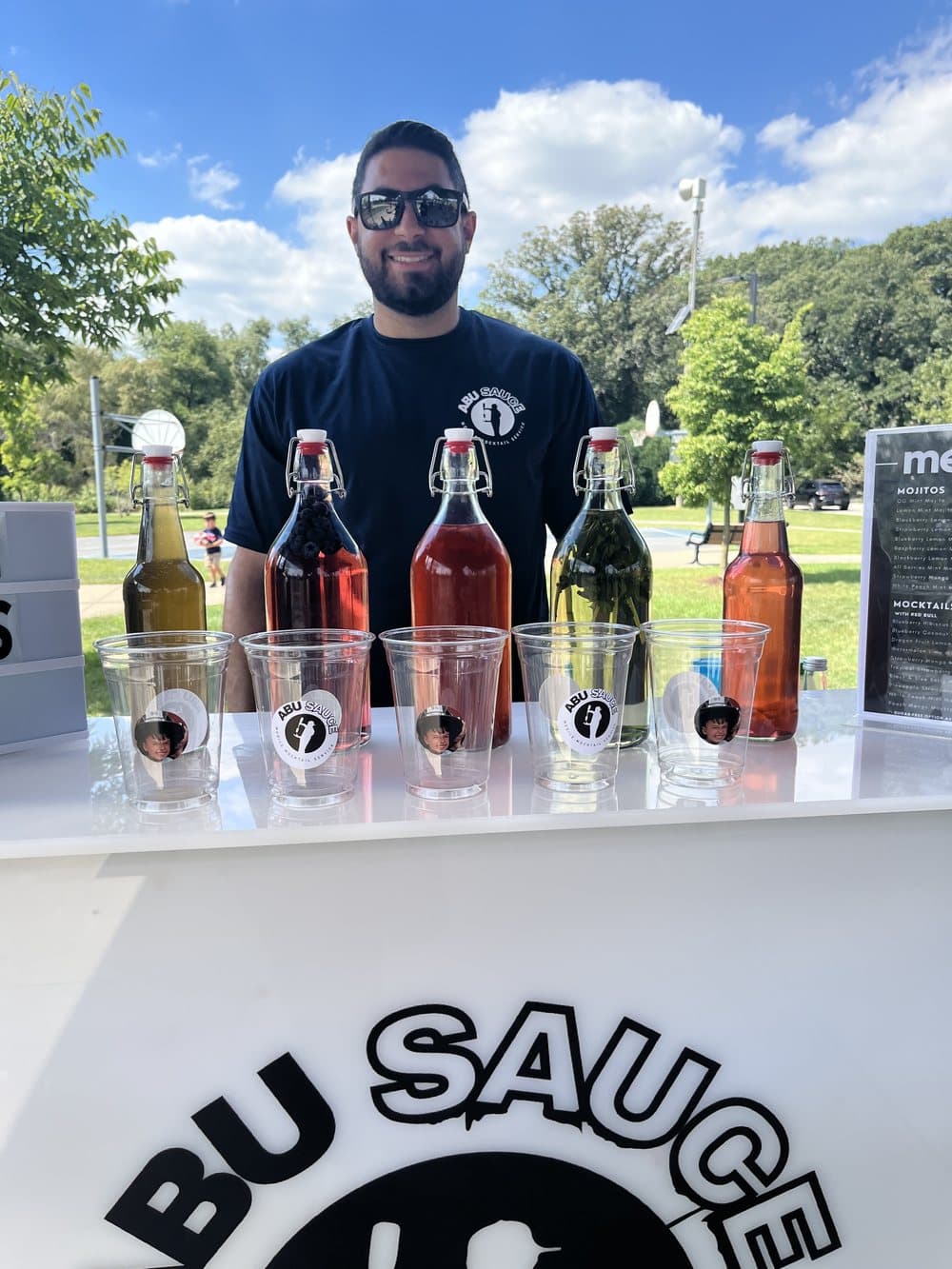 An Abu Sauce mixologist behind the branded bar with syrup bottles at an outdoor event