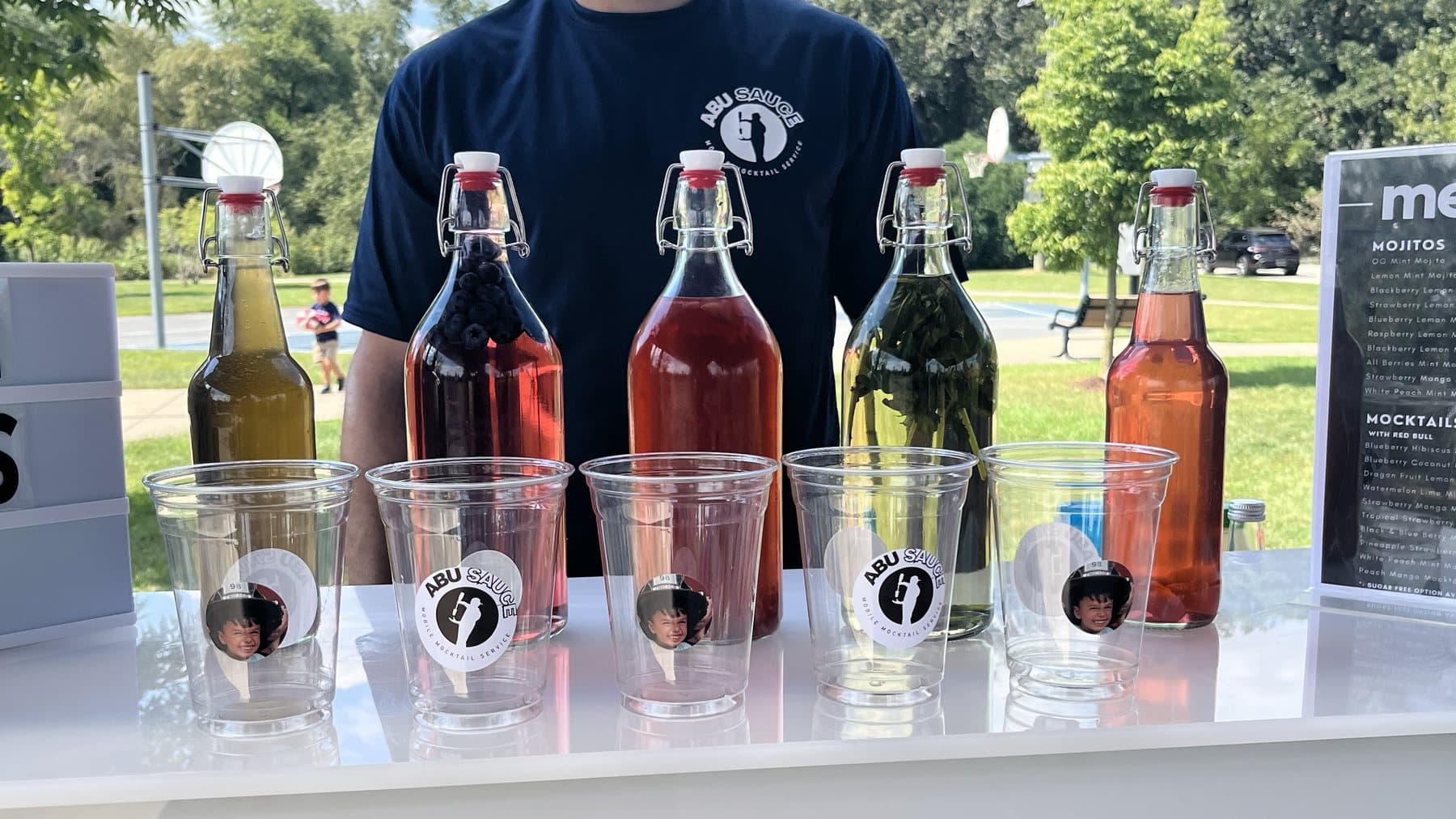 An Abu Sauce mixologist behind the branded bar with syrup bottles at an outdoor event